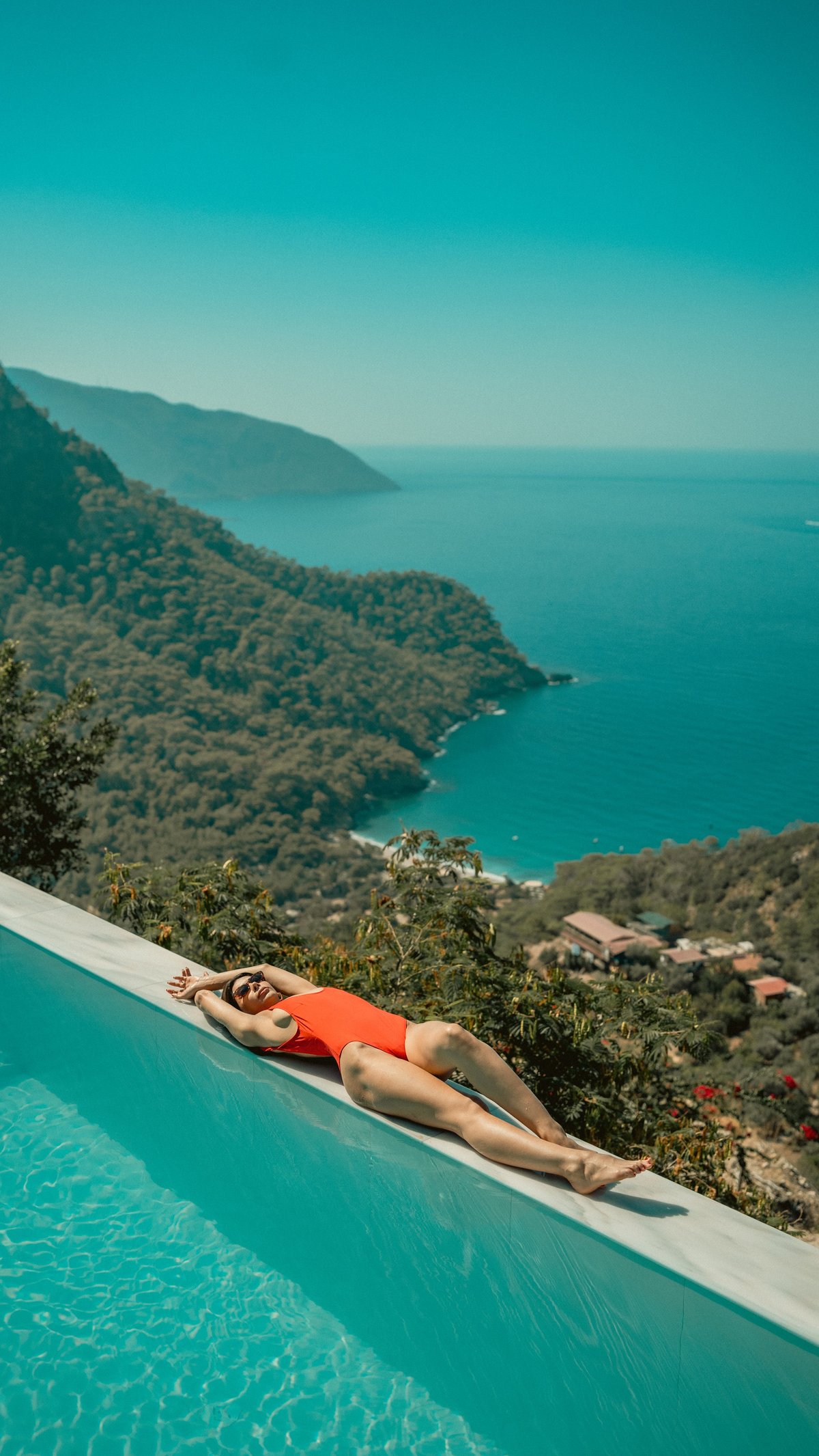 An infinity pool overlooking a lush green coastal landscape and clear blue sea